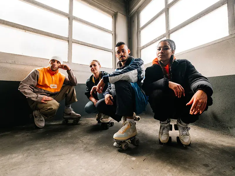 A group of four individuals posing in a casual indoor space with roller skates on