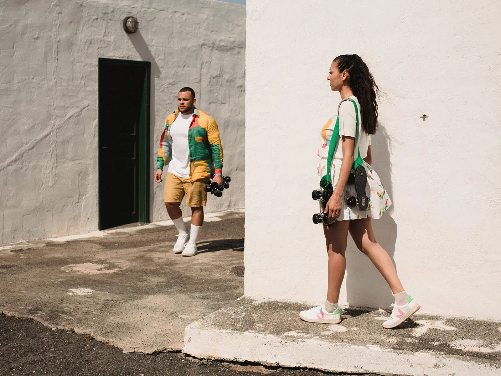 a man and a woman wandering in the city holding their roller skates